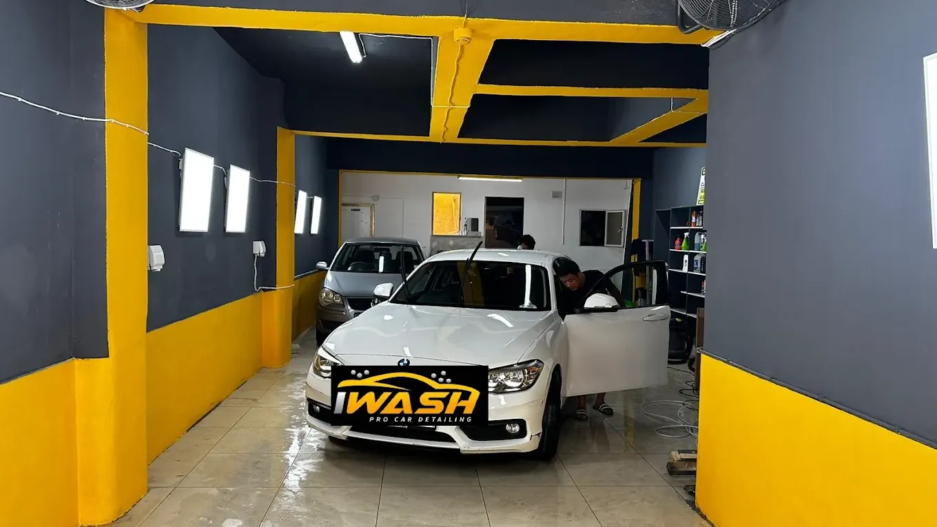 The iWash bay in Gżira, graphite walls with yellow beams, a white BMW being worked on with its door open