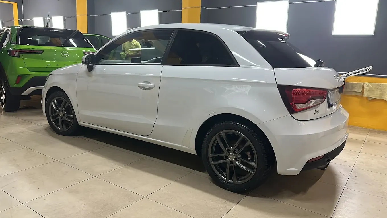 A white Audi A1 parked in the bay beside a green SUV, paintwork clean and reflective